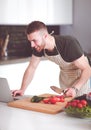 Portrait of man cooking vegetable in the kitchen while looking at a laptop computer on the table Royalty Free Stock Photo