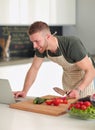 Portrait of man cooking vegetable in the kitchen while looking at a laptop computer on the table Royalty Free Stock Photo