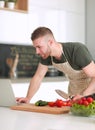 Portrait of man cooking vegetable in the kitchen while looking at a laptop computer on the table Royalty Free Stock Photo