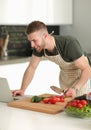 Portrait of man cooking vegetable in the kitchen while looking at a laptop computer on the table Royalty Free Stock Photo