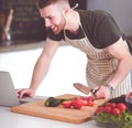 Portrait of man cooking vegetable in the kitchen while looking at a laptop computer on the table Royalty Free Stock Photo