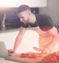 Portrait of man cooking vegetable in the kitchen while looking at a laptop computer on the table Royalty Free Stock Photo