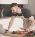 Portrait of man cooking vegetable in the kitchen while looking at a laptop computer on the table Royalty Free Stock Photo