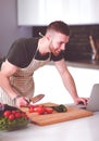 Portrait of man cooking vegetable in the kitchen while looking at a laptop computer on the table Royalty Free Stock Photo