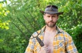 Portrait of man in cowboy hat. Serious cowboy holding hayfork. Cowboy in garden natural background