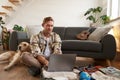 Portrait of man with dog, sitting on floor, has suitcase and laptop opened, booking or buying online, planning holiday Royalty Free Stock Photo