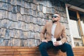 Portrait man in fashionable style with cup of coffee sitting outdoors, copy space on stone wall Royalty Free Stock Photo