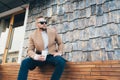 Portrait man in fashionable style with cup of coffee sitting outdoors, copy space on stone wall Royalty Free Stock Photo