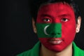 Portrait of a man with the flag of the Maldives painted on his face on black background.