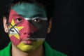 Portrait of a man with the flag of the Mozambique painted on his face on black background.