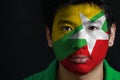 Portrait of a man with the flag of the Myanmar painted on his face on black background.