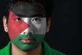 Portrait of a man with the flag of the Palestine painted on his face on black background.