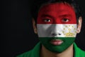 Portrait of a man with the flag of the Tajikistan painted on his face on black background.