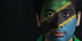 Portrait of a man with the flag of the Tanzania painted on his face on black background.