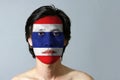 Portrait of a man with the flag of the Thailand painted on his face on black background.