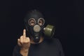 Portrait of man in gas mask on dark background, shows middle fingers sign by one hands
