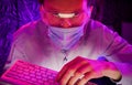 Portrait of a man in glasses and a medical mask sitting with a keyboard in front of the monitor Royalty Free Stock Photo