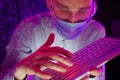 Portrait of a man in glasses and a medical mask sitting with a keyboard in front of the monitor Royalty Free Stock Photo