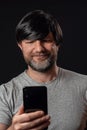 Portrait of a man with grey and black beard and long black hairs. Black background. Male dressed in grey t-shirt, smiling