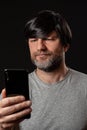 Portrait of a man with grey and black beard and long black hairs. Black background. Male dressed in grey t-shirt. Holding and
