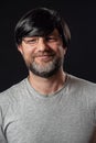 Portrait of a man with grey and black beard and long black hairs. Black background. Male dressed in grey t-shirt, wearing glasses