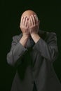 Portrait of a man in grey suit on dark background hands cover his face in grief. Male in his 40s with bald head and grey beard