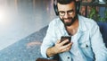 Portrait of man in headphones sitting in cafe, listening to music, watching video, webinar on smartphone, mobile phone Royalty Free Stock Photo