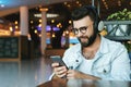 Portrait of man in headphones sitting in cafe, listening to music, watching video, webinar on smartphone, mobile phone Royalty Free Stock Photo