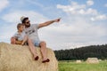 portrait of man and his little son sitting on round haystack in a green field on sunny summer day. Royalty Free Stock Photo