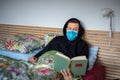 Portrait of man lying and reading a book in bed with sickness and facial mask Covid-19