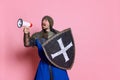 Portrait of man, medieval warrior or knight in armor with shield shouting in megaphone isolated over pink studio Royalty Free Stock Photo