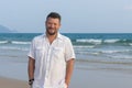 Portrait of a man with a middle beard in a white shirt, on the beach