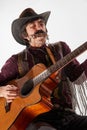 Portrait of man with moustaches in country style clothes playing guitar and harmonica, performing isolated over white Royalty Free Stock Photo