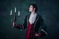 Portrait of man in noble medieval costume in image of vampire holding candles over dark green background