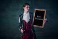 Portrait of man in noble medieval costume in image of vampire holding picture frame isolated over dark green background