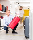 Portrait of man picking new big plastic luggage bag with wheels