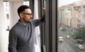 Portrait of man sad and depressed standing at window in despair at home