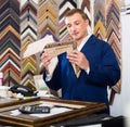 Portrait of man seller working with picture frames in atelier