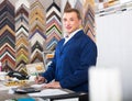 Portrait of man seller working with picture frames in atelier