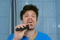 Portrait of man shaves beard using electric razor in bathroom looking at camera. Royalty Free Stock Photo