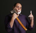 Portrait man shaving with big axe and foam on his face