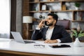 Portrait of man sitting at desk in chair having phone call with business partners in new modern office. Royalty Free Stock Photo