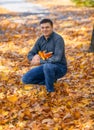 Portrait of a man, he is sitting in a glade and picking yellow maple leaves, a bright sunny day in an autumn park Royalty Free Stock Photo