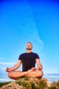 Portrait of the man sitting on a rock in the lotus position against blue sky. Royalty Free Stock Photo