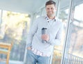 Portrait of man smiling and standing holding a flask. Attractive male leaning against a window inside his home with a Royalty Free Stock Photo