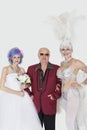 Portrait of man standing arms in arms with senior showgirl and daughter in wedding dress over gray background