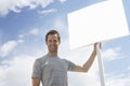 Portrait of man with standing by blank sign against cloudy sky Royalty Free Stock Photo