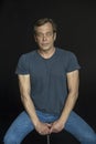 Portrait of a man in a Studio 40-50 years old in a blue t-shirt with strong hands on a black blurry background. Maybe he`s just a