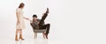 Portrait of man in a suit, cap with moustaches sitting on chair over white background. Woman pouring him coffee