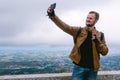 Portrait of a man use smartphone take selfie. dressed in a stylish brown leather jacket and jeans. backpack watches and biker